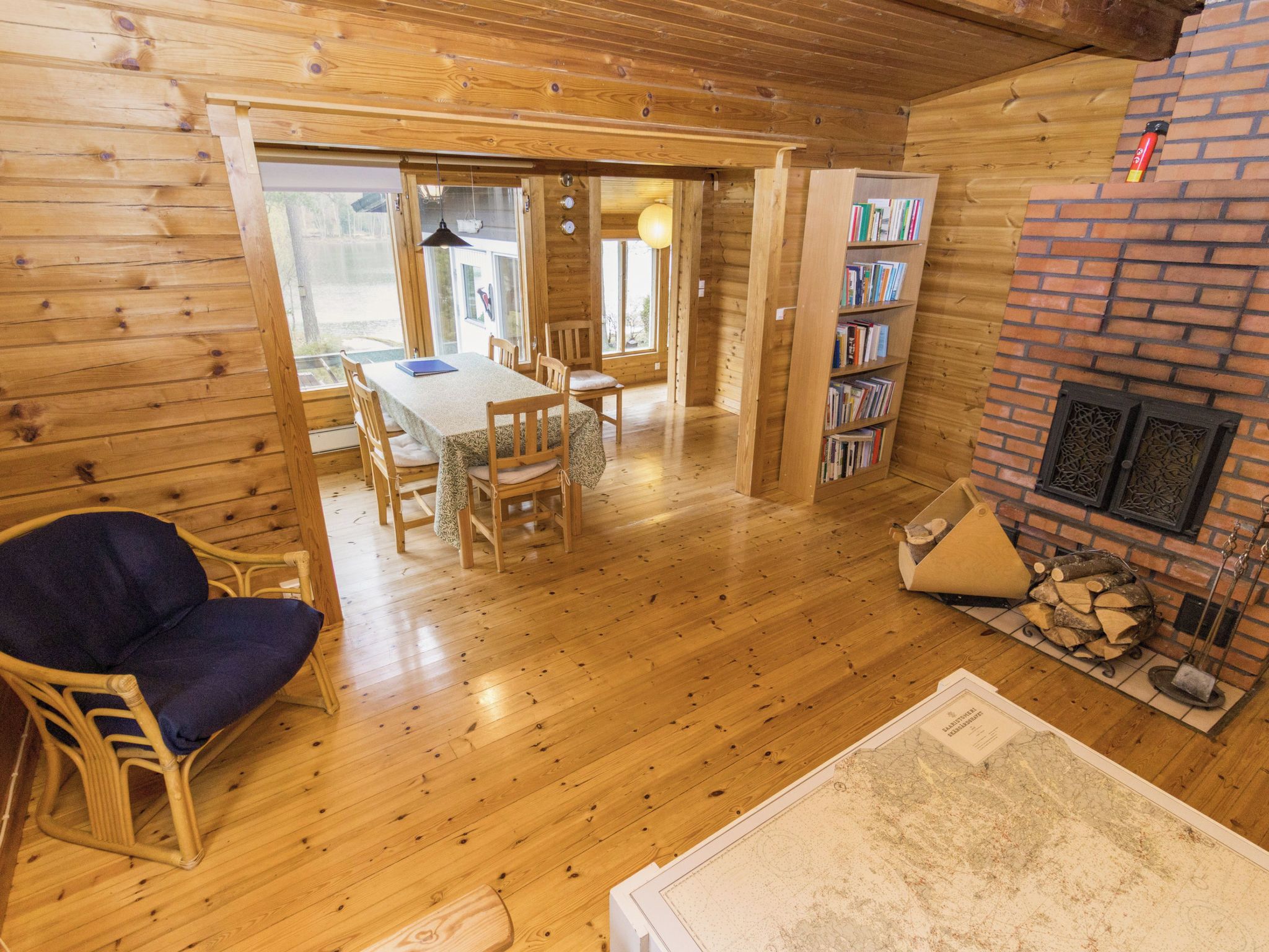 A wooden interior with a dining area, a bookshelf, and a fireplace.