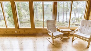 Ein Interieur einer Hütte mit großen Fenstern, Holzboden und zwei weißen Polsterstühlen.