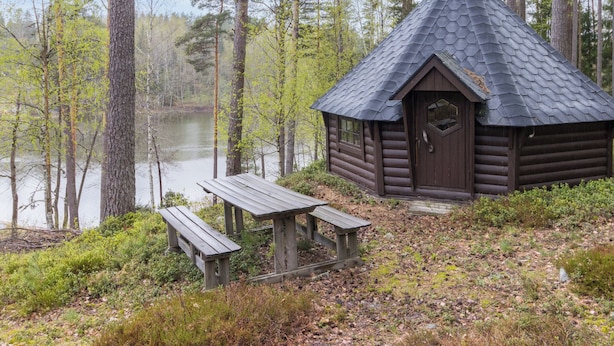 Eine Blockhütte mit sechseckigem Dach, einer Holztür und einer Bank.