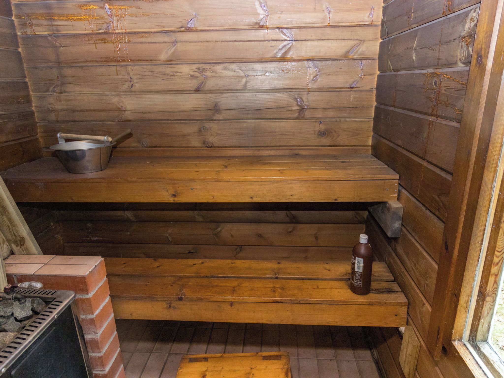 Ein Holzblockhaus-Innenraum mit Kamin aus Ziegelsteinen, einem Metalltopf auf einer Ablagefläche und einer Flasche am Boden.