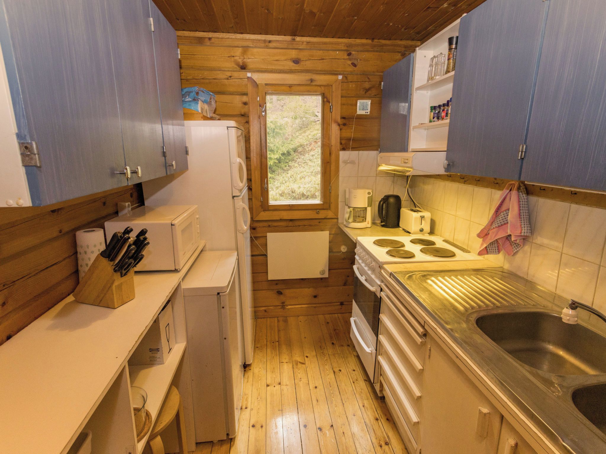 A compact kitchen with wooden walls, a window, a sink, and basic appliances.