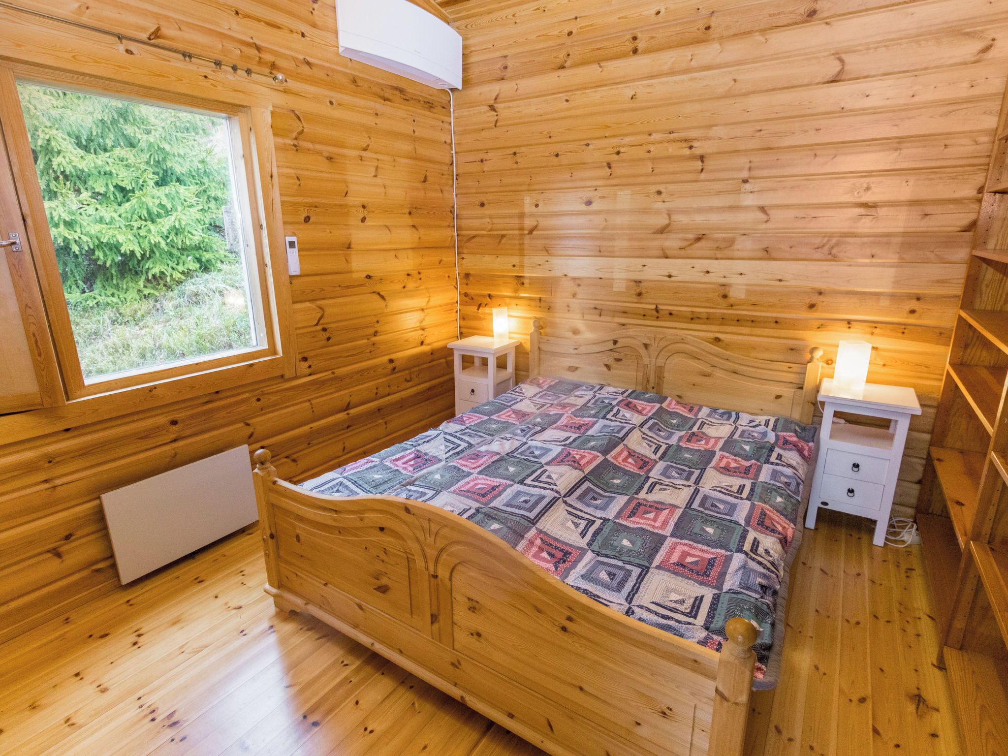 Une chambre dans une cabane en bois, comprenant un lit, deux tables de chevet, une fenêtre et un appareil de climatisation.