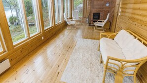 Ein Blockhaus-Interieur mit großen Fenstern, einem Kamin und Korbmöbeln.