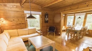 Ein Holzblockhaus-Innenraum mit einer Couch, einem Esstisch, Stühlen, einer Hängelampe und einem Bild an der Wand.