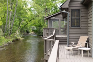 Eine Hütte mit einer Terrasse mit Blick auf einen Fluss, umgeben von Bäumen.