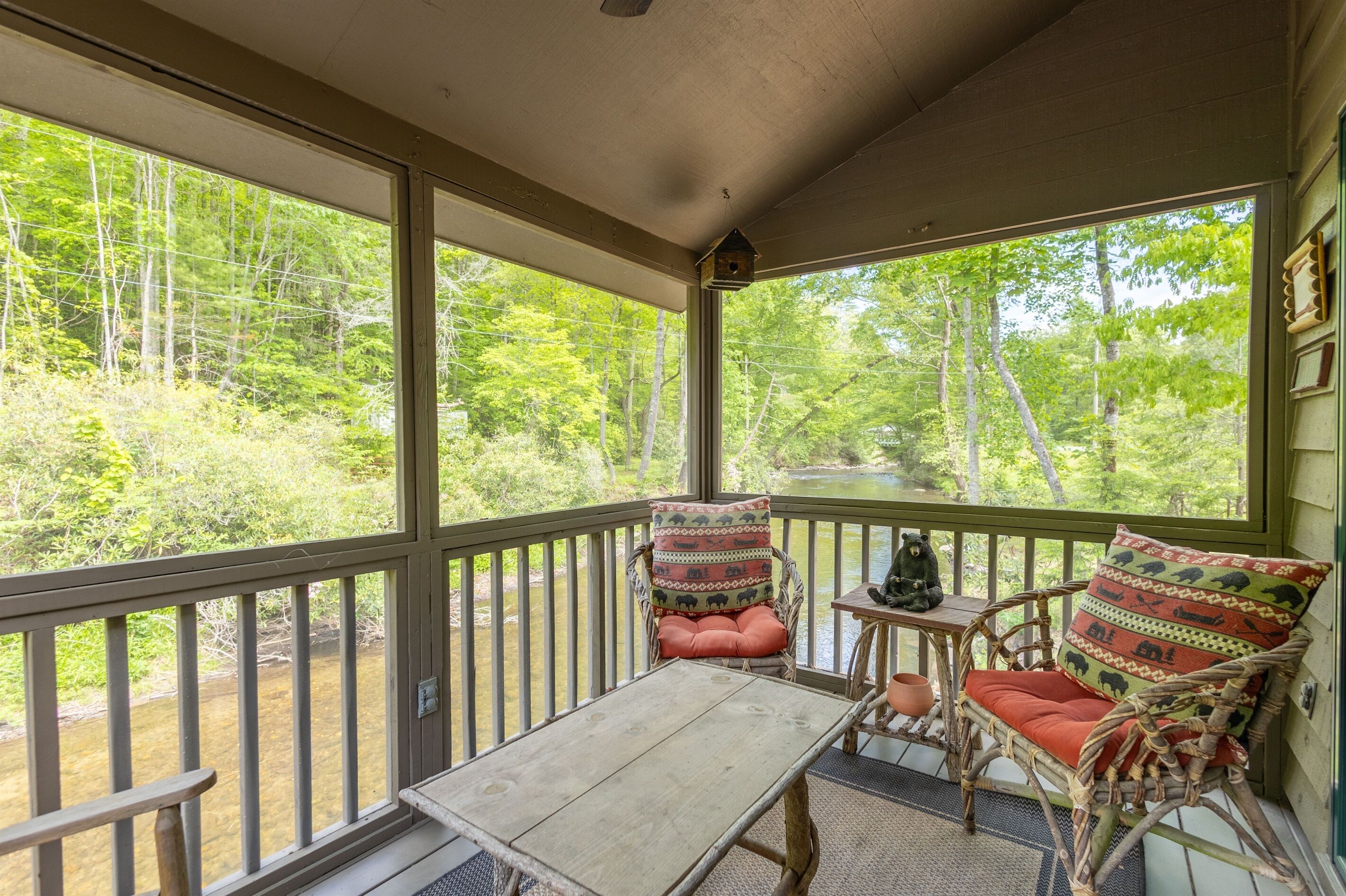 A porch with wicker furniture, a table, and a view of a forested area.