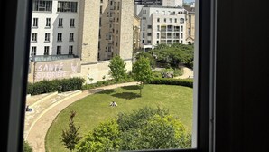 A view through a window of a building with a courtyard, featuring a mix of modern and traditional architecture, including a prominent stone tower. - Charming apartment in the heart of Paris (Île de France)