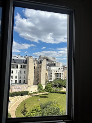 A view through a window of a building with a courtyard, featuring a mix of modern and traditional architecture, including a prominent stone tower. - Charming apartment in the heart of Paris (Île de France)