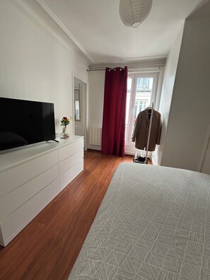 A bedroom with a bed, a dresser, a TV, a red curtain, and a coat rack. - Charming apartment in the heart of Paris (Île de France)
