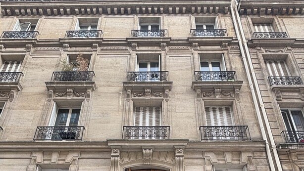 A multi-story building with a central entrance, balconies with wrought iron railings, and storefronts with awnings. - Charming apartment in the heart of Paris (Île de France)