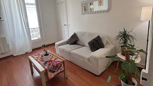 A living room with a sofa, a coffee table, a potted plant, and a mirror on the wall. - Charming apartment in the heart of Paris (Île de France)