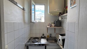 A compact kitchen with white tiles, a small refrigerator, a gas stove, a sink, and a window with a view of buildings. - Charming apartment in the heart of Paris (Île de France)