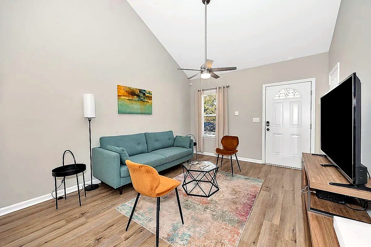 A living room with a sofa, two chairs, a TV, and a ceiling fan.