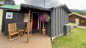 Une cabane en bois rustique, dotée d’un porche, d’une porte rouge et d’une enseigne indiquant qu’il s’agit du « gîte de Petit Ours ».