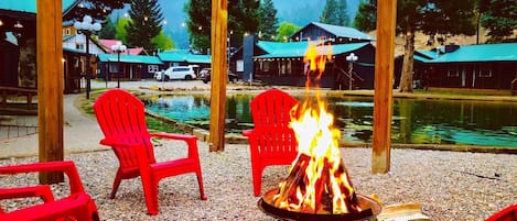 Un foyer avec des chaises rouges disposées autour, une étendue d’eau et des cabanes en arrière-plan.