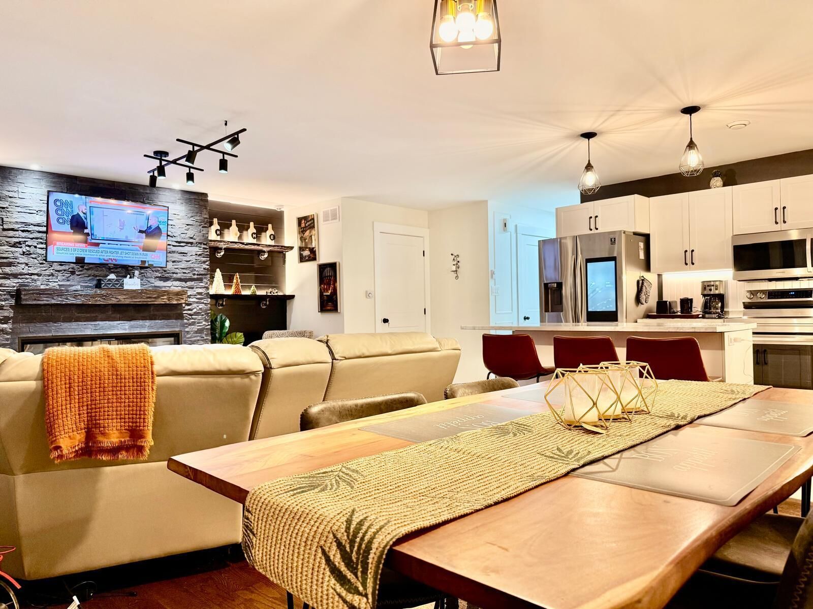 Een moderne woonkamer met een open haard, een aan de muur bevestigde televisie en een eethoek met een houten tafel en stoelen.