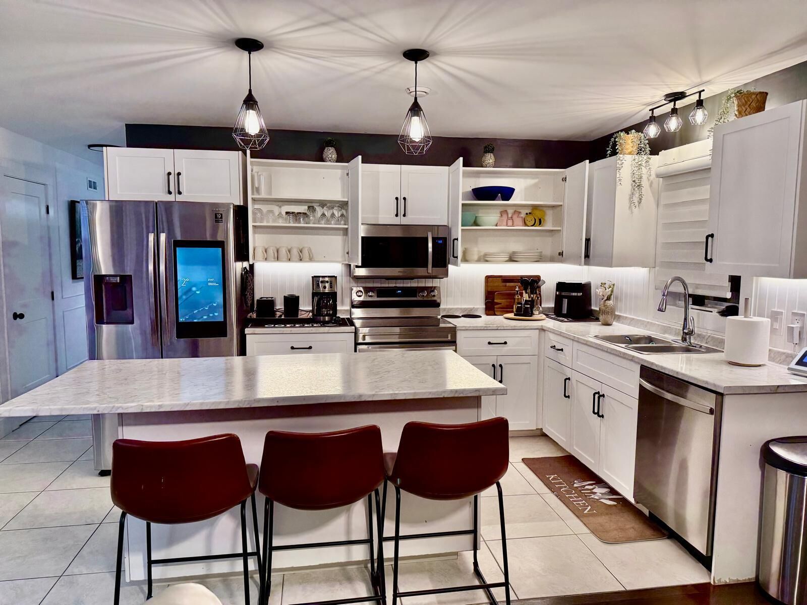 Een moderne keuken met een centraal eiland, roestvrijstalen apparatuur en rode barstoelen.