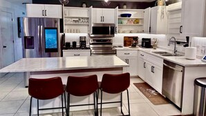 A modern kitchen with a central island, stainless steel appliances, and red bar stools. - High-end haven where Serenity meets Style and Fun| 5mins to airport| 5 car slots (Moncton)