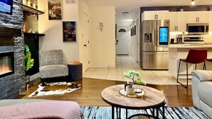 A modern living room with a fireplace, a dining area, and a kitchen with stainless steel appliances. - High-end haven where Serenity meets Style and Fun| 5mins to airport| 5 car slots (Moncton)
