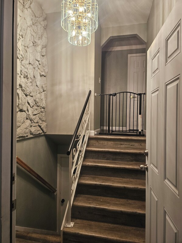Una escalera de madera con barandilla de metal y pared de piedra.