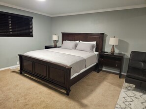 Un dormitorio con una cama grande, dos mesitas de noche, una silla y una ventana con persianas.