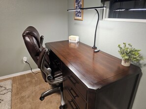Un escritorio de madera con una silla, una planta pequeña y una lámpara de escritorio.