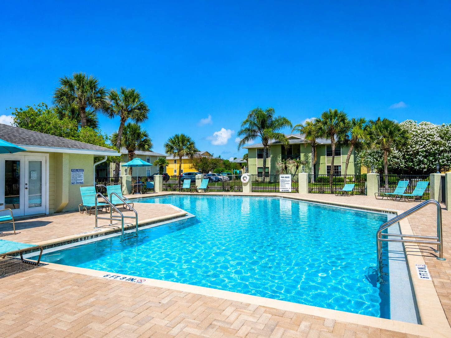 A clear blue pool with a shallow end, surrounded by lounge chairs and palm trees.