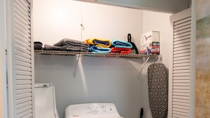 A laundry room with a washing machine, dryer, and a shelf with folded clothes. - Cozy Florida Retreat | Pool | Beach | Comfort (St. Augustine)