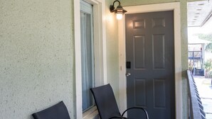A porch with three chairs, a door, and a light fixture. - Cozy Florida Retreat | Pool | Beach | Comfort (St. Augustine)
