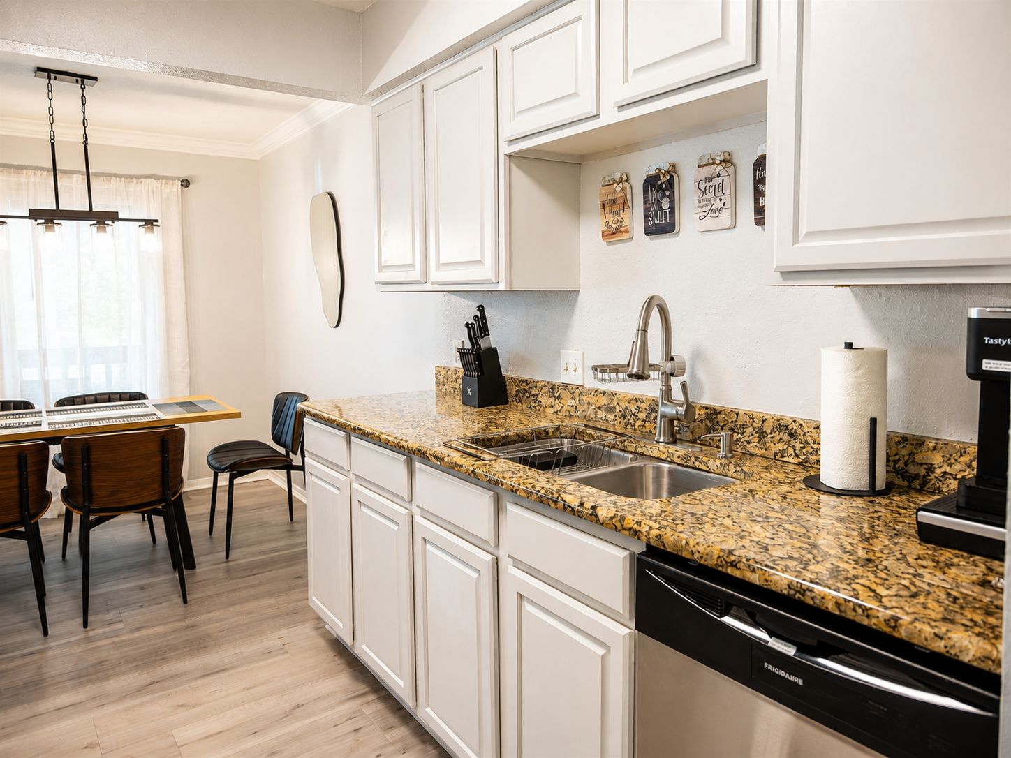 Une cuisine moderne avec des meubles blancs, un plan de travail en granit, un lave-vaisselle encastré et un coin repas comprenant une table et des chaises.