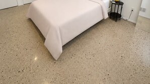 Un dormitorio con cama, paredes blancas, una mesita y una mesita de noche.