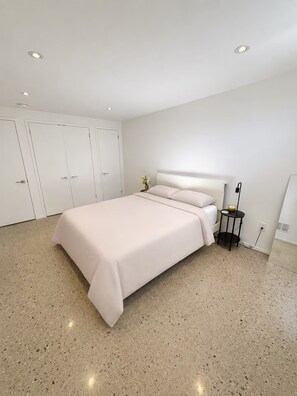 Une chambre à coucher avec un lit, des murs blancs, une petite table et une table de chevet.