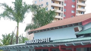 Een Starbucks koffiezaak met terras, palmbomen en een rood luifel.