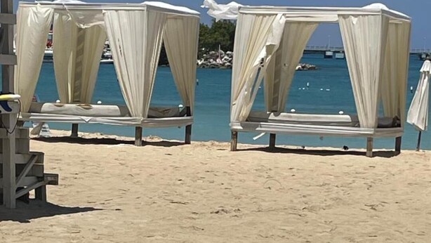 Een strand met twee witte luifeltenten en een houten constructie.