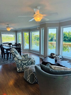 A spacious room with a dining area, large windows, and a ceiling fan.