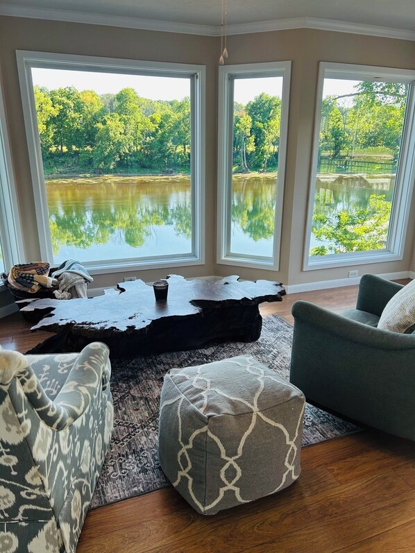 A living room with a large window overlooking a lake, a wooden coffee table, and two sofas.