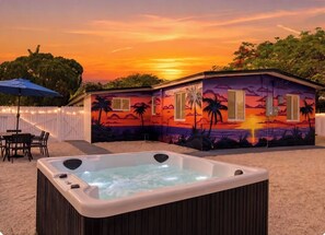 Un jacuzzi en un patio trasero con un mural de atardecer en la casa.