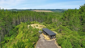 A cabin with a flat roof, surrounded by dense forest, with a clear sky above. - Luxury Bush Retreat with Outdoor Bath, Birds, Trails & Wine Country  | Waimauku. (Helensville)