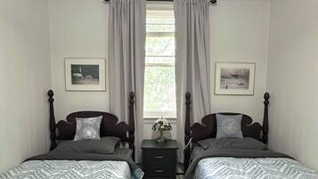 Une chambre double avec deux lits, une table de chevet, une lampe et une fenêtre avec des rideaux.