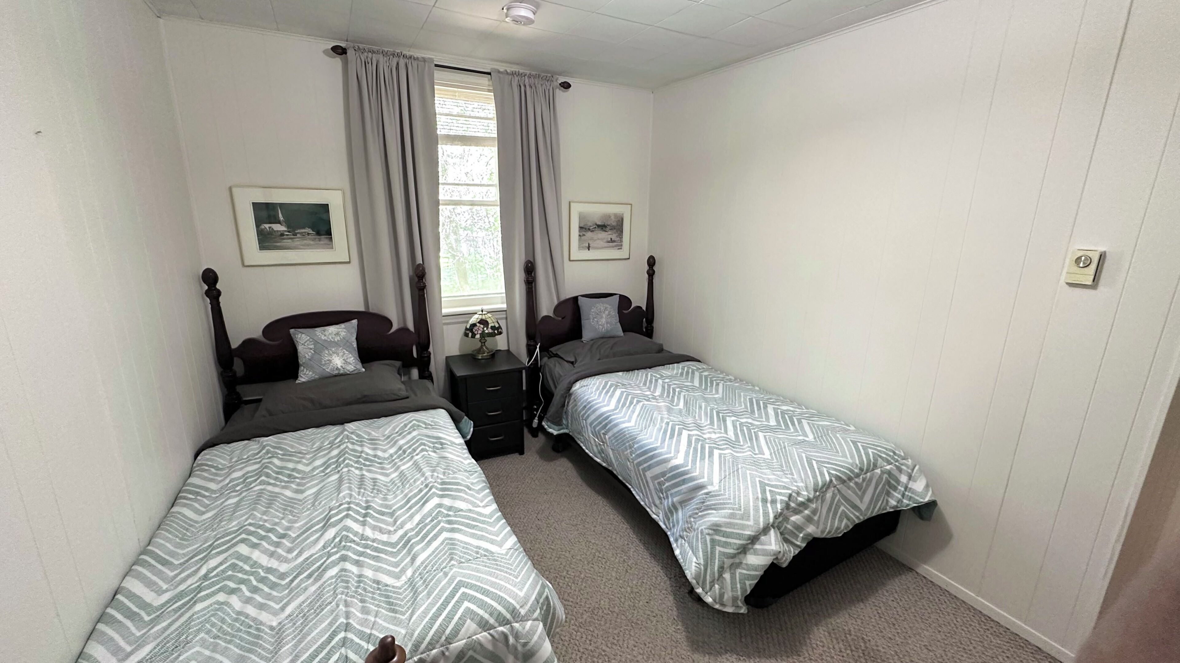 A bedroom with two single beds, a nightstand, a lamp, and two framed pictures on the wall.