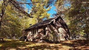 Un chalet rustique en pierre, doté d’une cheminée, entouré d’arbres.