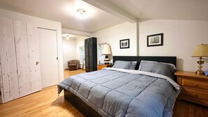 A bedroom with a bed, a nightstand, a lamp, and a chair. - Falcon Retreats  – Kestrel (Sharbot Lake)