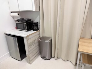 Eine kleine Küchenzeile mit Mikrowelle, Kaffeemaschine und Papierkorb.