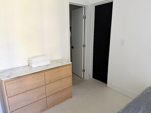 Ein Zimmer mit einem hölzernen Schminktisch, einem weißen Handtuch darauf, einer geschlossenen Tür und einem Lichtschalter an der Wand.