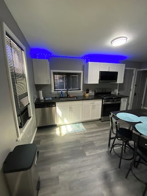 A modern kitchen with white cabinets, a black countertop, a built-in oven, and a dining area with a glass table.