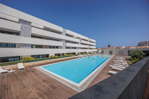 Ein modernes Gebäude mit Pool auf dem Dach, Liegestühlen und blauem Himmel.