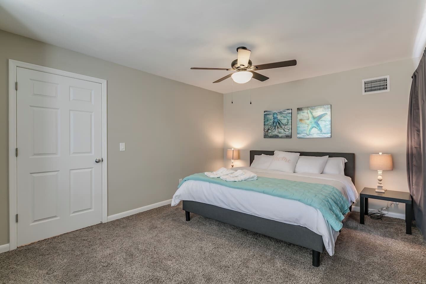 Quarto com uma cama, duas luminárias laterais, um ventilador de teto e obras de arte na parede.