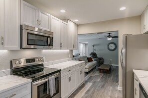 A modern kitchen with stainless steel appliances, white cabinetry, and a dining area with a sofa and coffee table. - Central Melb Accessible 5bd/3ba Pool-Sleeps 14! (Melbourne)