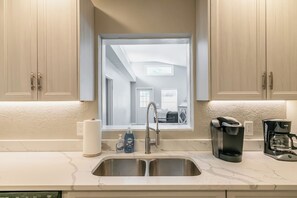 A kitchen with a double sink, a coffee maker, and a view of a bedroom through a window. - Central Melb Accessible 5bd/3ba Pool-Sleeps 14! (Melbourne)