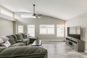 A living room with a sectional sofa, a flat-screen TV, a ceiling fan, and large windows. - Central Melb Accessible 5bd/3ba Pool-Sleeps 14! (Melbourne)